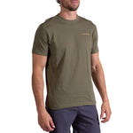 A man wears the La Sportiva Psychotomic T-Shirt Men's, an olive green organic cotton short-sleeve tee with a small yellow logo on the left chest, paired with dark shorts, standing against a white background.