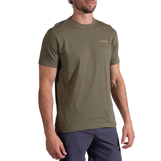 A man wears the La Sportiva Psychotomic T-Shirt Men's, an olive green organic cotton short-sleeve tee with a small yellow logo on the left chest, paired with dark shorts, standing against a white background.