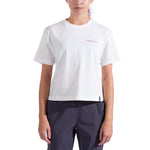 A woman wears the La Sportiva Redgarden Crop T-Shirt—a plain white organic cotton tee with a small red LA SPORTIVA logo on the left chest—paired with dark pants, standing against a white background.