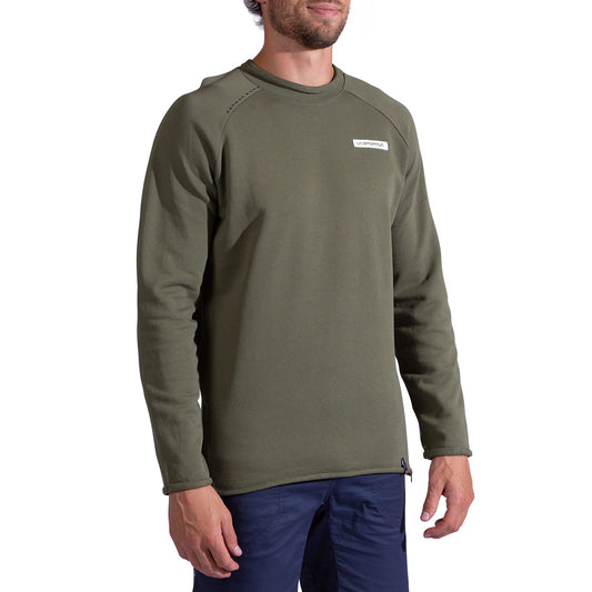 A man faces forward with a slight smile, wearing the La Sportiva Tufa Sweater Men's in olive green—crafted from organic cotton and featuring a small rectangular logo on the left chest—paired with blue pants.