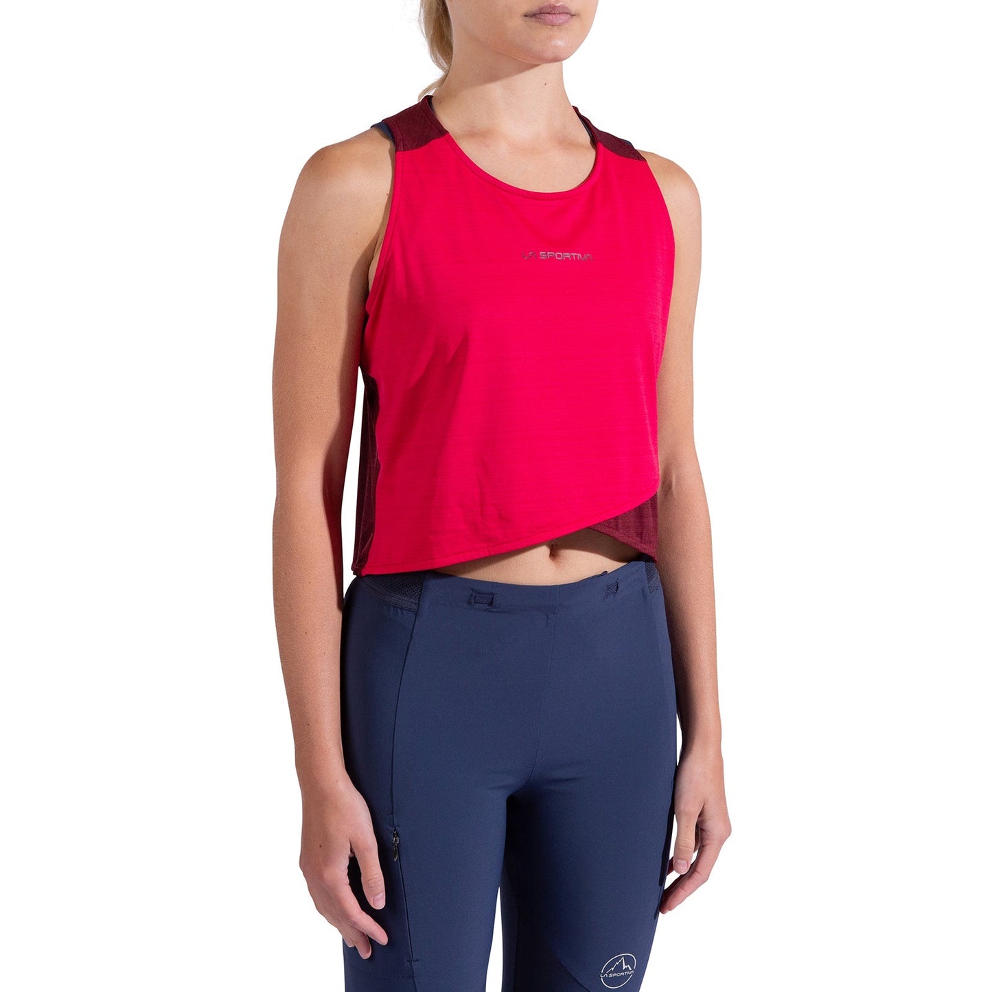 A person wearing a La Sportiva Sunfire Tank Women's in bright pink with a slightly asymmetrical hem and navy blue leggings featuring a small logo on the left thigh stands against a plain white background.