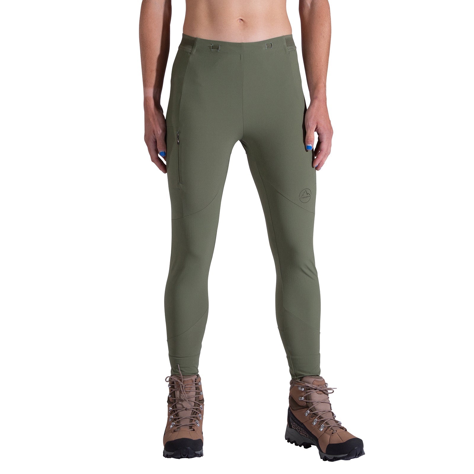 A woman faces forward against a white background, wearing La Sportiva Camino Tight Pants Women's in olive green with a zippered right thigh pocket and durable fabric, paired with brown hiking boots.