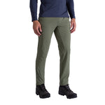 A person wears La Sportiva Trail Guard Pants Men's in olive green, with a navy long-sleeve shirt and black hiking boots, standing against a plain white background—ideal for trail enthusiasts.