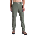 A woman wears La Sportiva West Crest Pants in olive green, featuring zippered pockets, along with brown hiking boots, standing with arms relaxed at her sides against a plain white background.