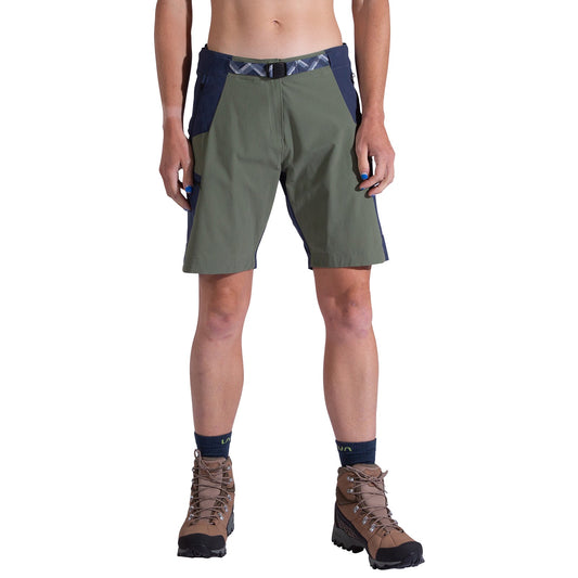 A woman wearing La Sportiva West Crest Shorts in olive green and navy, navy socks, and brown hiking boots stands facing forward against a white background. Only her body from the waist to feet is visible.