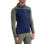 A man wears the La Sportiva Big Wall Pullover Hoody Men's, featuring a fitted design with olive green sleeves and sides, a navy blue front panel, hood, chest zipper, and subtle red accents.