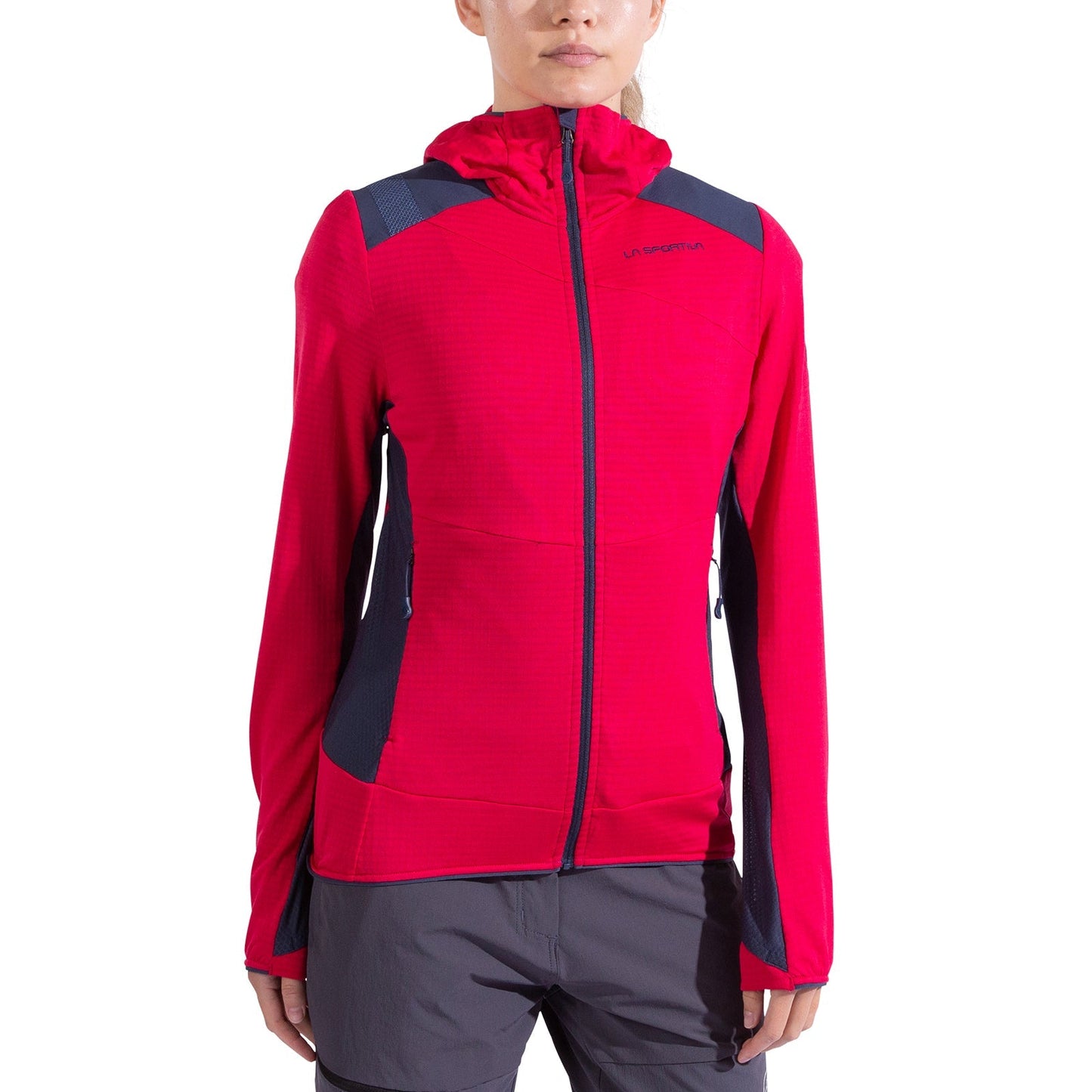 A woman wears the La Sportiva Aequilibrium Thermal Hoody in bright pink with dark gray accents and Polartec Power Grid fabric, featuring a front zipper and cuff thumb holes, paired with gray shorts. The background is plain white.