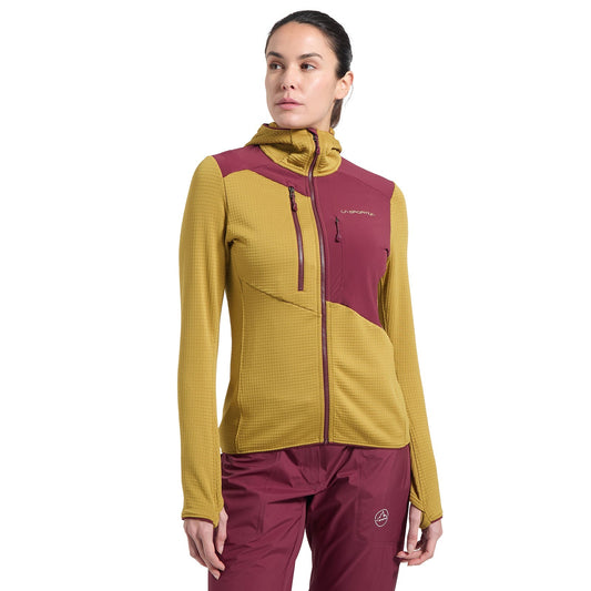 A woman stands against a white background wearing the La Sportiva Lucendro Thermal Hoody Women's in mustard yellow and maroon, crafted with Polartec Power Grid, paired with matching maroon pants for an athletic midlayer look.