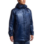 A person models the La Sportiva Supercouloir Primaloft Parka Men's—a shiny, dark blue alpine insulation jacket with a front zipper and subtle logo—standing relaxed against a plain white background.