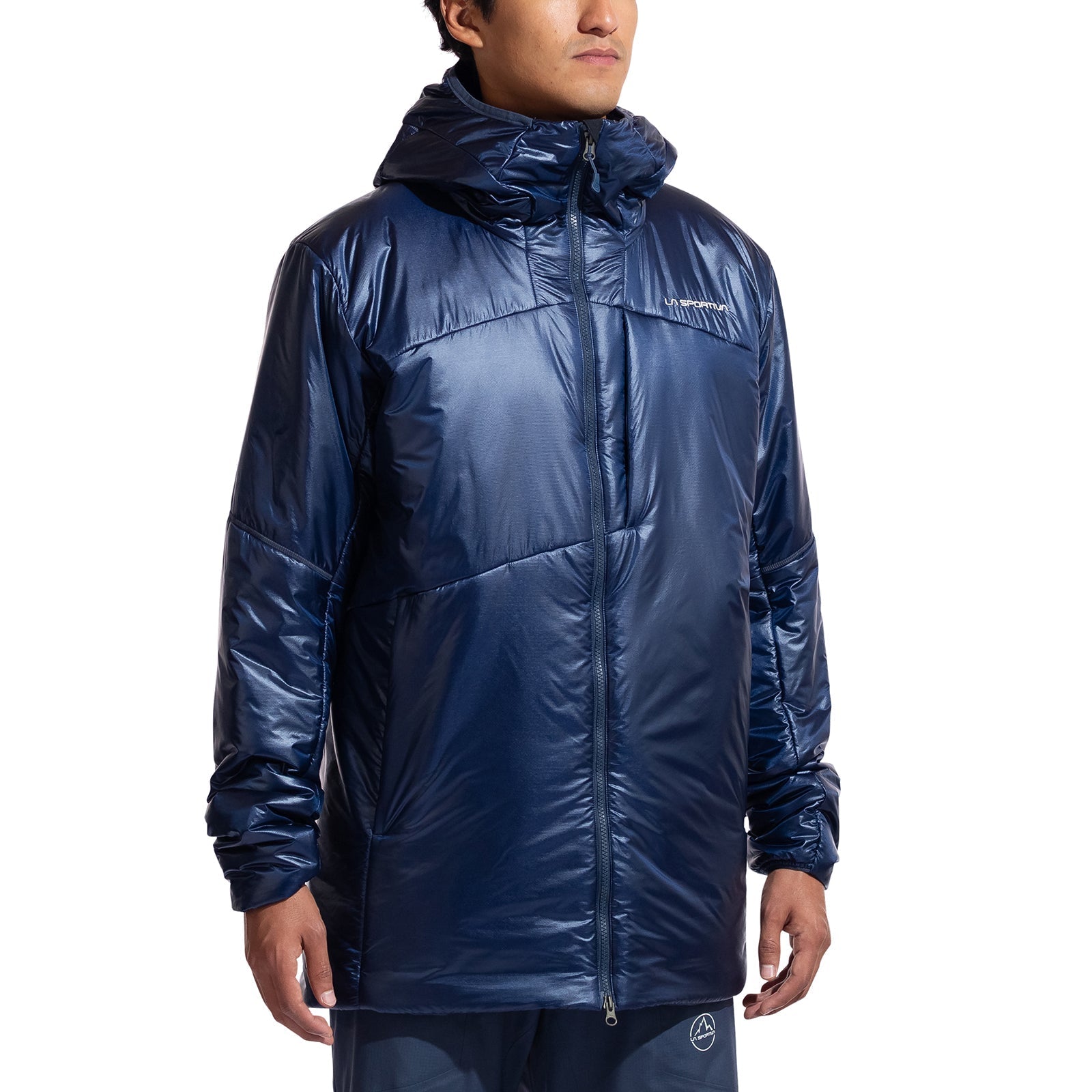A person models the La Sportiva Supercouloir Primaloft Parka Men's—a shiny, dark blue alpine insulation jacket with a front zipper and subtle logo—standing relaxed against a plain white background.