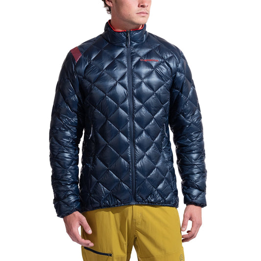 A man wearing the La Sportiva Lumina 100 Down Jacket Men's, a shiny dark blue insulated coat, and yellow pants stands against a plain white background.