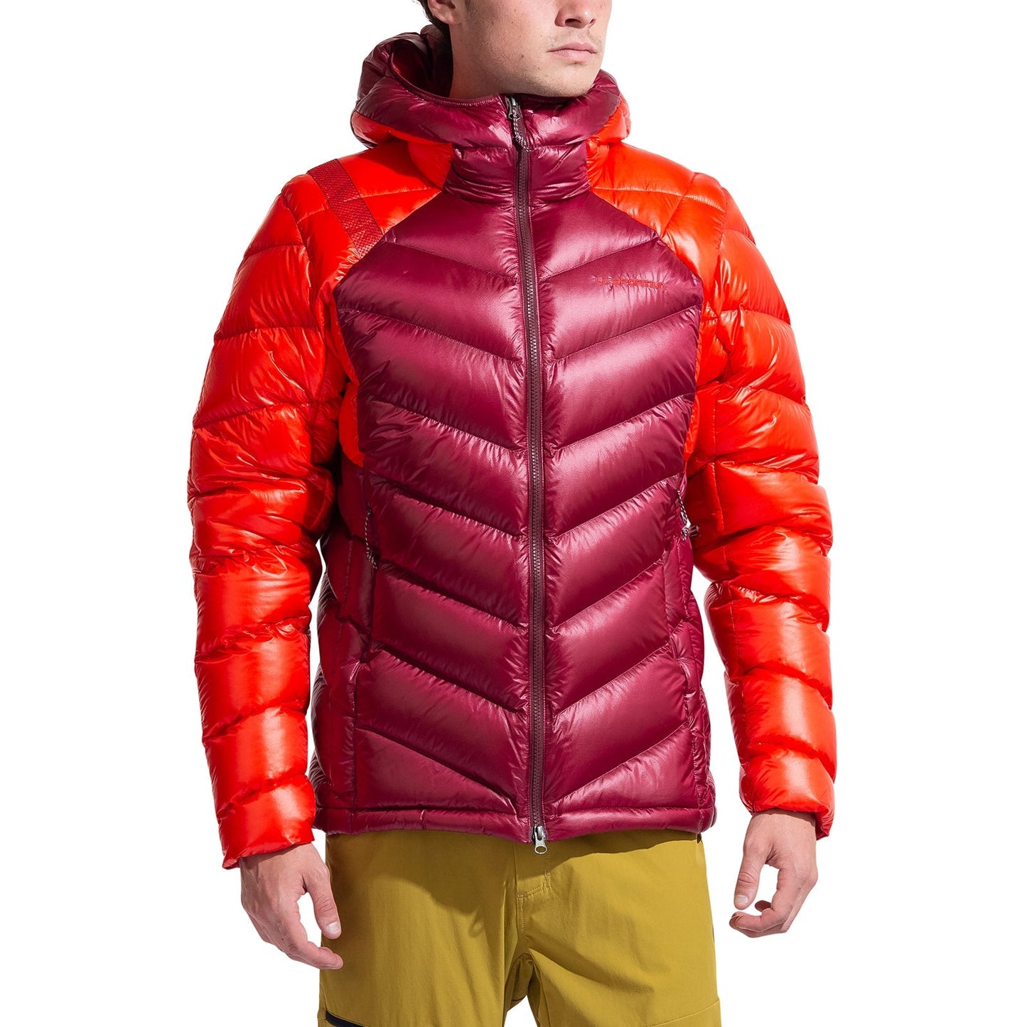 A person wears the La Sportiva Lumina 300 Down Jacket Men's—a shiny, quilted, lightweight, hooded down jacket with a maroon center and bright orange sleeves and shoulders—paired with yellow pants. This jacket is packable and provides excellent thermal performance.