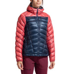 A person wears the La Sportiva Lumina 200 Down Jacket Women's—a lightweight, packable jacket with coral sleeves and hood, navy blue chest and body, hood up and zipped—ideal insulation for cool days.