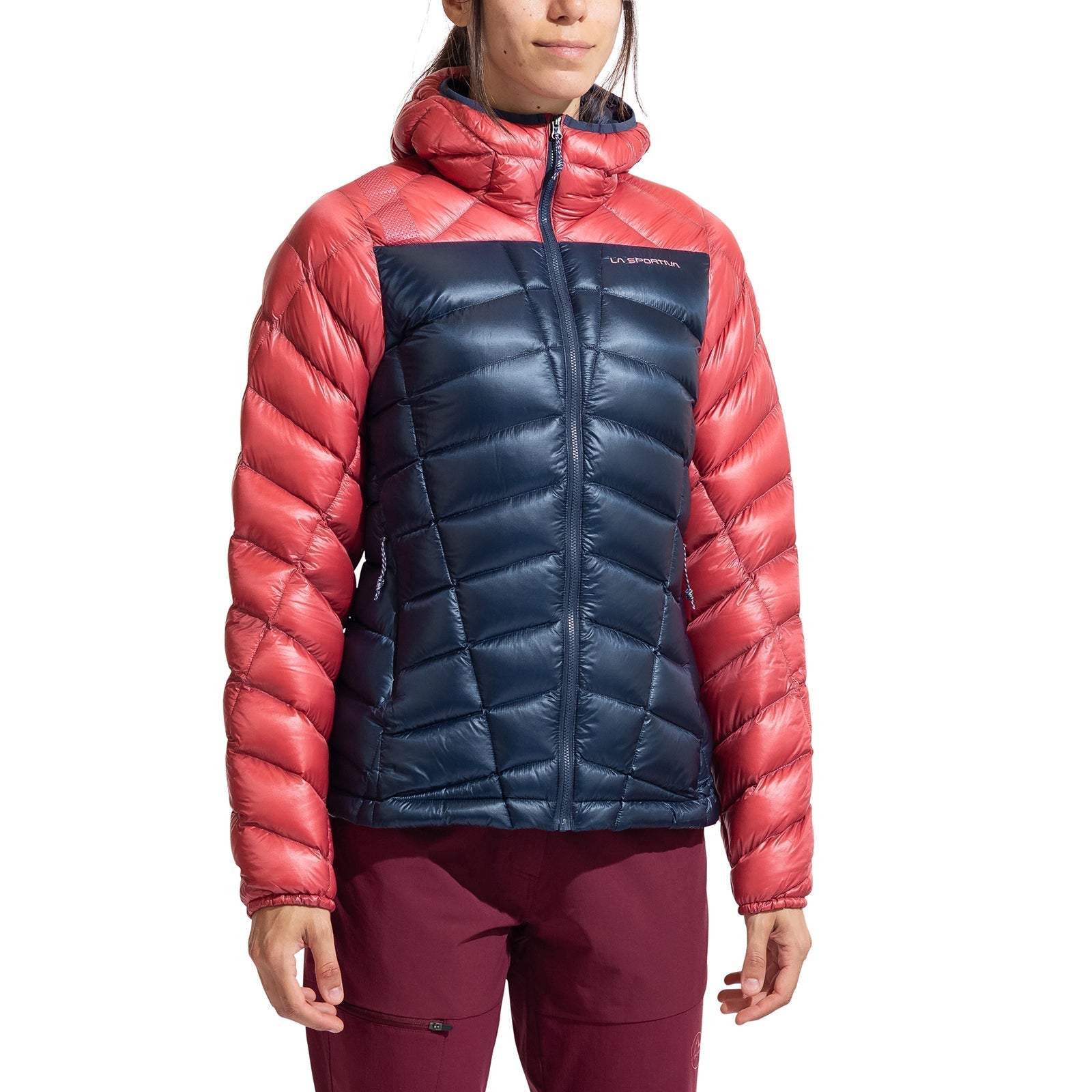 A person wears the La Sportiva Lumina 200 Down Jacket Women's—a lightweight, packable jacket with coral sleeves and hood, navy blue chest and body, hood up and zipped—ideal insulation for cool days.
