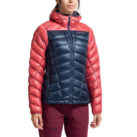 A person wears the La Sportiva Lumina 200 Down Jacket Women's—a lightweight, packable jacket with coral sleeves and hood, navy blue chest and body, hood up and zipped—ideal insulation for cool days.