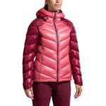 A woman wears the La Sportiva Lumina 300 Down Jacket, a shiny, two-tone pink and burgundy, chevron-patterned hooded jacket with matching burgundy pants, posed against a plain white background.