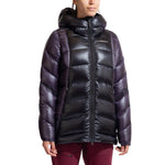 A person wears a shiny, black and dark purple La Sportiva Supercouloir Down Parka Women's with horizontal quilting, zipped up and paired with burgundy pants. This packable down jacket suits high-altitude climbing style against a white background.