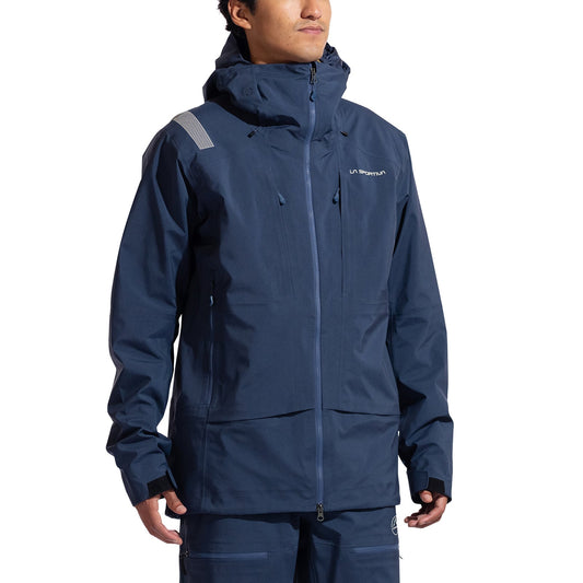 A person wears the La Sportiva Sender GTX Performance Jacket Men's in dark blue with matching pants for ski touring. The GORE-TEX jacket has a high collar, visible zippers, and a small chest logo, set against a plain white background.