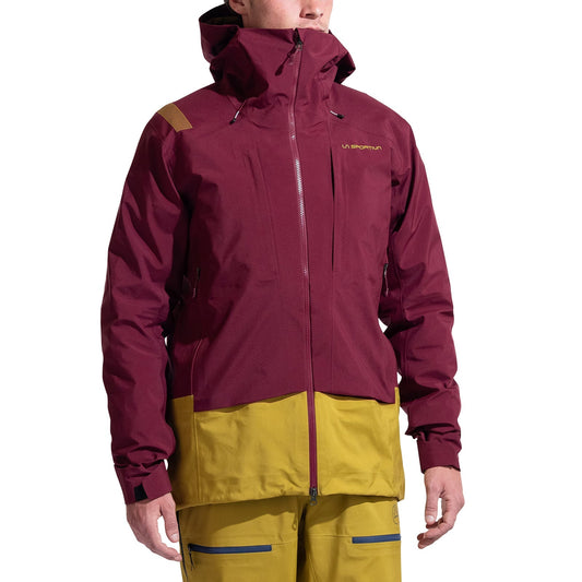 A person wearing the La Sportiva Sender GTX Performance Jacket Men's with a maroon upper and mustard yellow lower, featuring a hood, front zipper, chest pocket, and matching mustard yellow pants—ideal for ski touring.