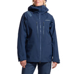A person wears the La Sportiva Supercouloir GTX Pro Jacket Women's in dark blue with matching pants, featuring zippers, chest pockets, and the La Sportiva logo on the chest. They stand with arms relaxed at their sides.
