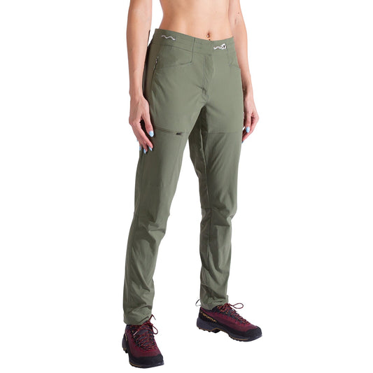 A woman wearing La Sportiva Machina Tech Pants in olive green—lightweight, fitted, harness-compatible with zipper pockets—and maroon hiking shoes stands against a white background.