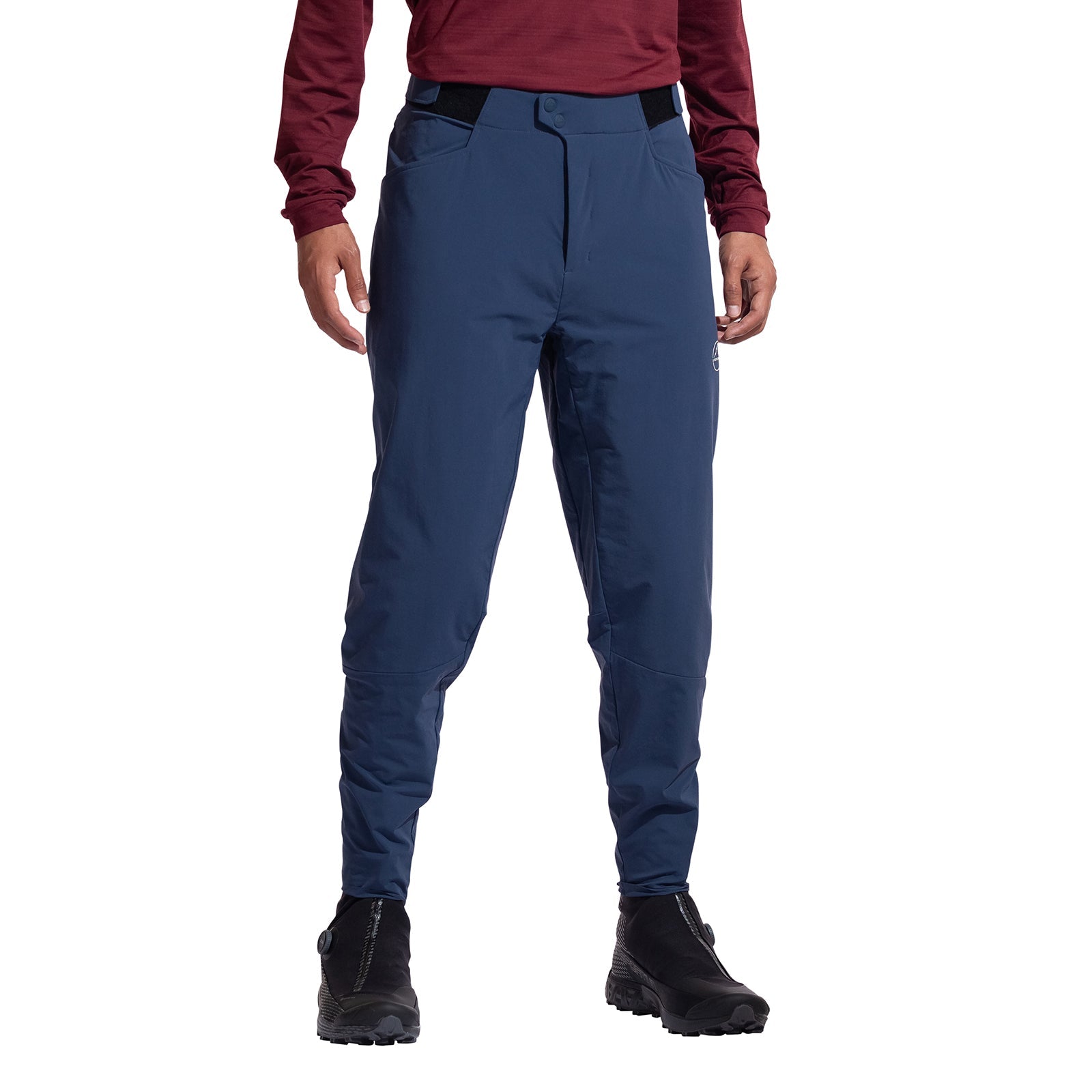 A person models the La Sportiva Nordend Primaloft Pants Men's in blue, paired with a maroon long-sleeve top and black hiking boots. Only the lower half of their body is visible against a white background.