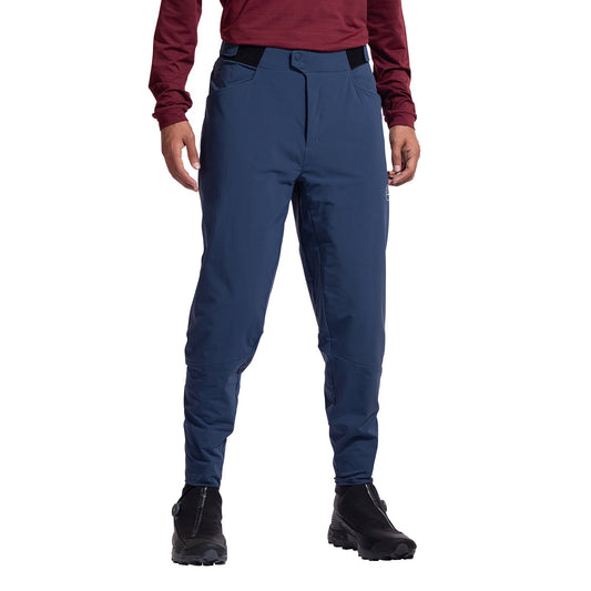 A person models the La Sportiva Nordend Primaloft Pants Men's in blue, paired with a maroon long-sleeve top and black hiking boots. Only the lower half of their body is visible against a white background.