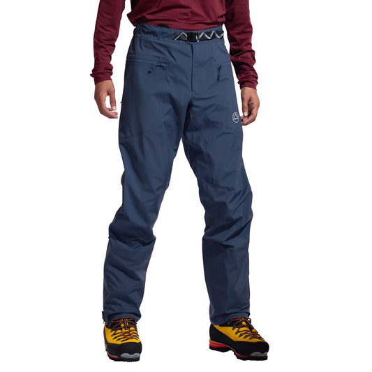 A person wearing La Sportiva Alpine Guide GTX Performance Pants Men's—waterproof, breathable pants with zippered pockets—is shown from the waist down, paired with yellow hiking boots, against a white background.