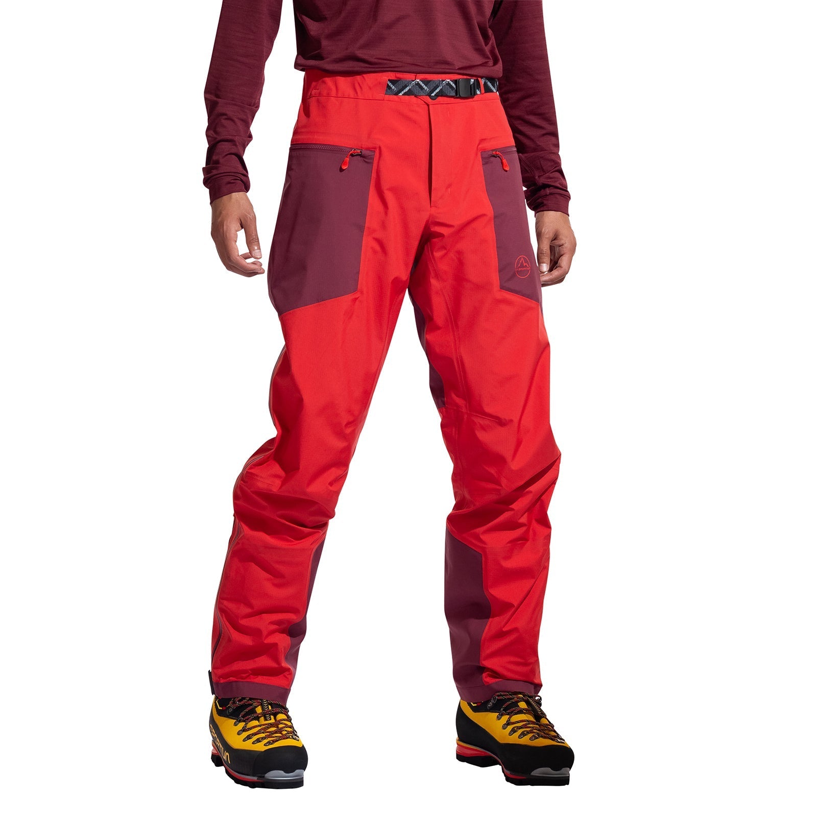 A person wearing La Sportiva Alpine Guide GTX Performance Pants Men's in bright red and maroon—waterproof, breathable, with zippered pockets—plus a maroon long-sleeve shirt and yellow, black, and red hiking boots stands against a white background.