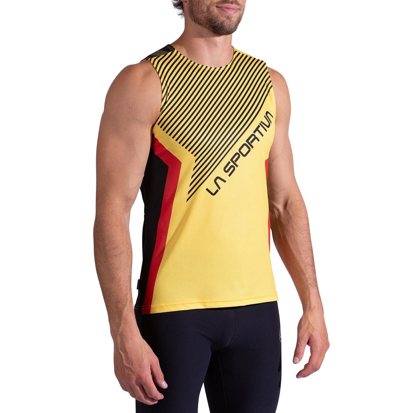 A man wearing the La Sportiva Flow Tank Men's—a sleeveless yellow trail running top with black diagonal stripes, red accents, and La Sportiva branding—paired with black leggings.