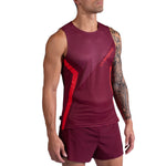 A man stands against a white background wearing the La Sportiva Flow Tank Men's in maroon with diagonal red accents and matching maroon shorts. His left arm features a tattoo sleeve.
