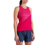 A woman wears a sleeveless red La Sportiva Flow Tank Women's top with diagonal stripes, made from recycled polyester, paired with navy blue athletic shorts, standing against a white background.