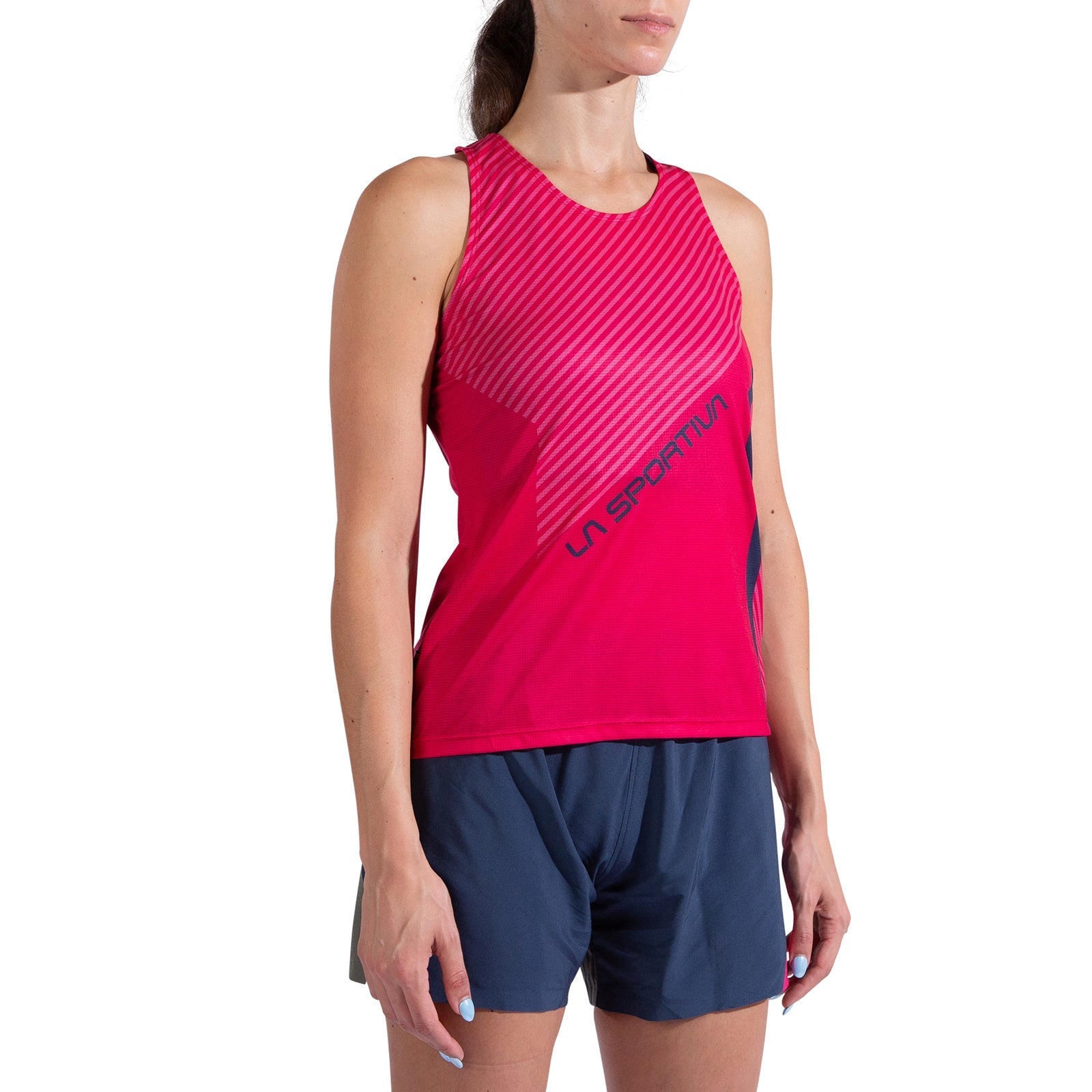 A woman wears a sleeveless red La Sportiva Flow Tank Women's top with diagonal stripes, made from recycled polyester, paired with navy blue athletic shorts, standing against a white background.