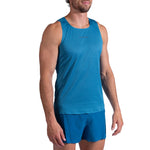 A man stands against a plain white background wearing the La Sportiva Pure Tank Men's—a sleeveless blue trail running top made from recycled polyester.