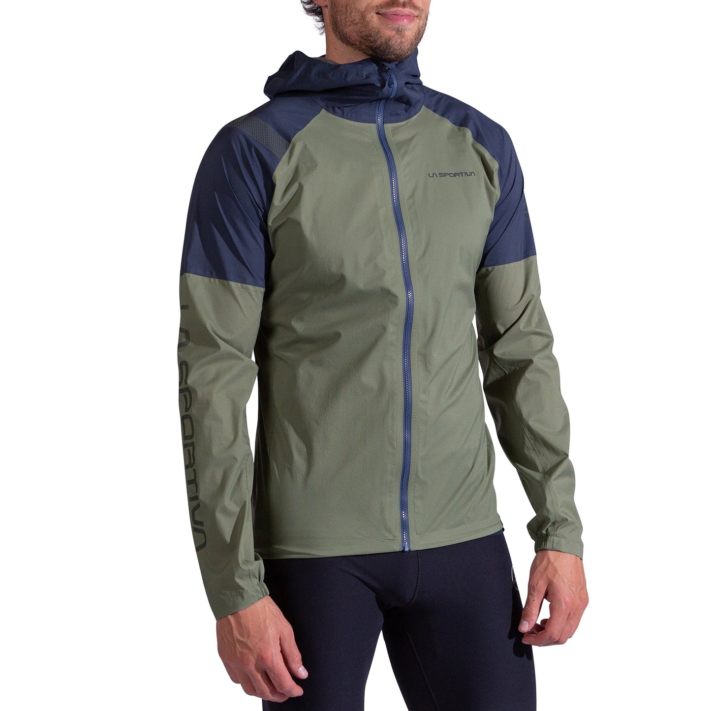A man wearing a race-ready La Sportiva Pocketshell Jacket Men's in olive green and navy with a front zipper, La Sportiva branding on the chest and left sleeve, and black leggings, stands against a plain white background.