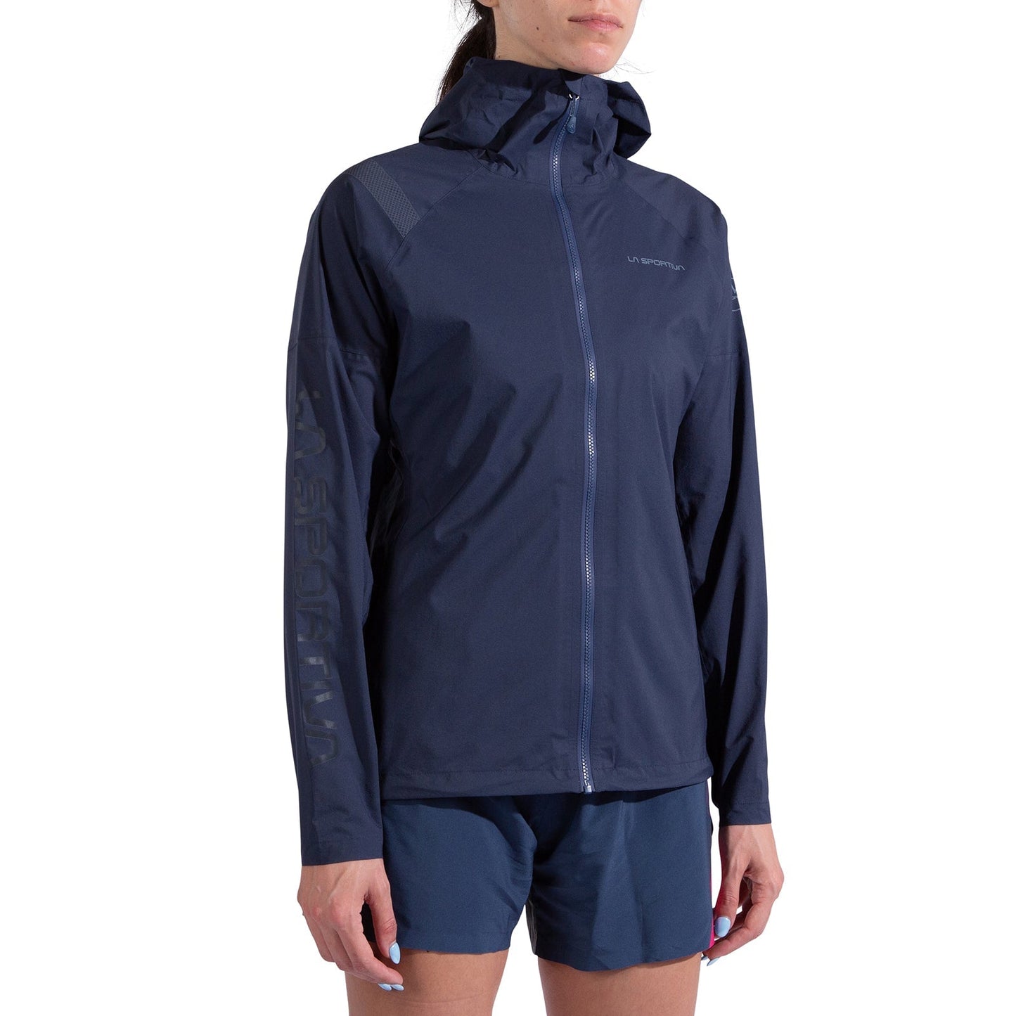 A woman wears the La Sportiva Pocketshell Jacket Women's in navy blue with a front zipper and matching shorts, standing against a plain white background.