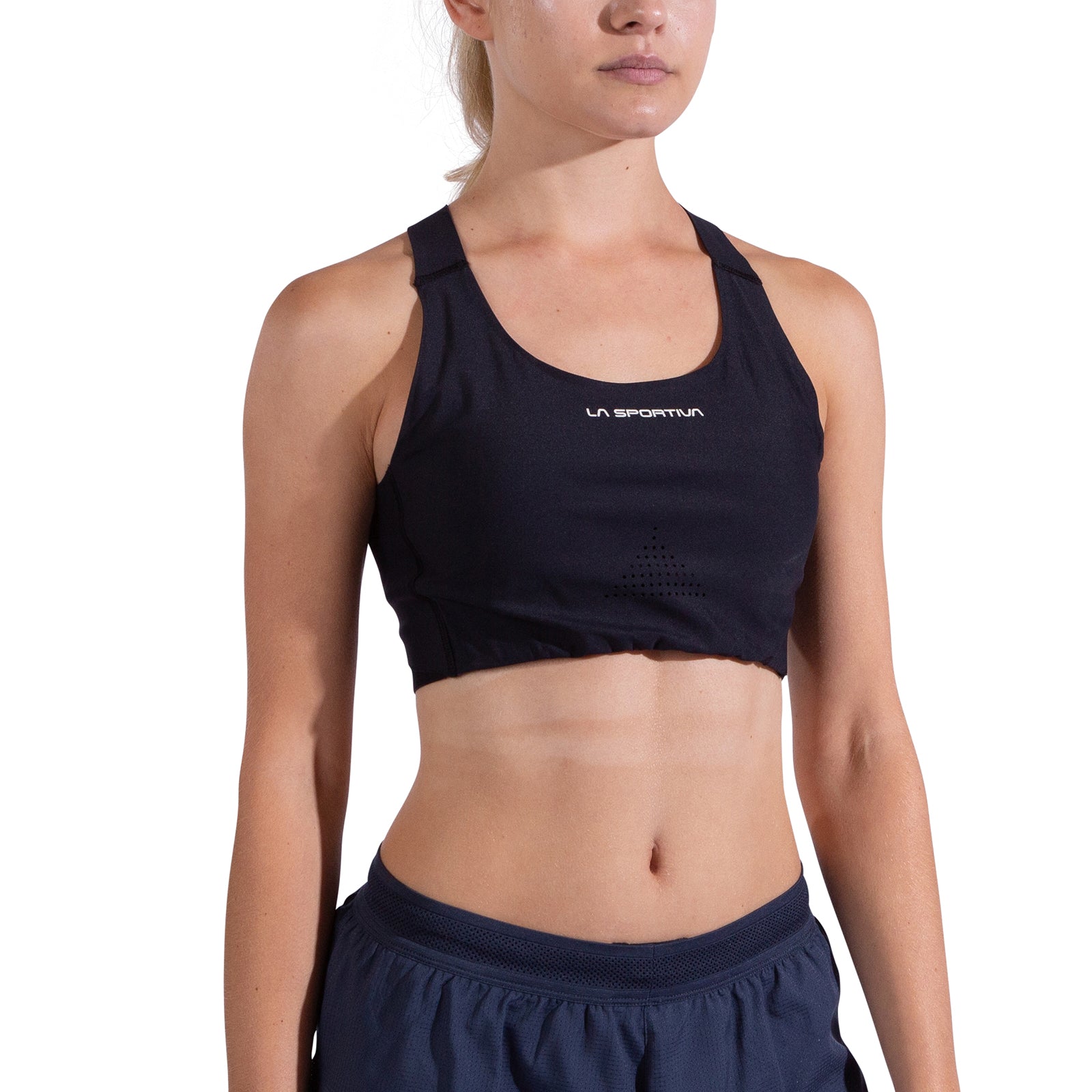 A woman in a black La Sportiva Pulse High Support Bra with crisscross straps and navy athletic shorts stands facing forward against a plain white background, her face partially out of frame.
