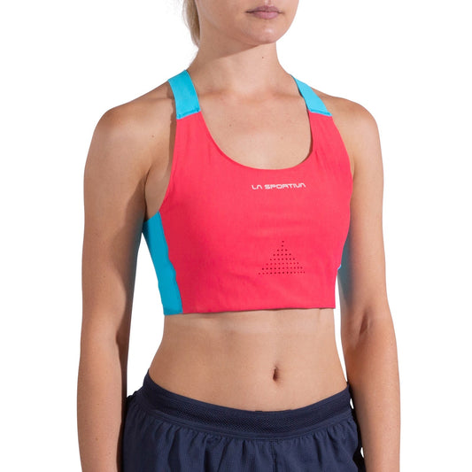 A woman wears the La Sportiva Pulse High Support Bra Women's in red and blue with crisscross straps, paired with navy athletic shorts. The image shows her from shoulders to waist against a plain white background.