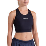 A woman models the La Sportiva Stash Bra Women's in black, paired with navy athletic shorts. Pictured from the waist up against a white background, this medium-support sports bra is perfect for trail running.