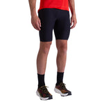 A person wearing a red shirt, La Sportiva Triumph Tight Shorts Men's in black, black socks, and black athletic shoes with yellow and red accents stands against a white background.