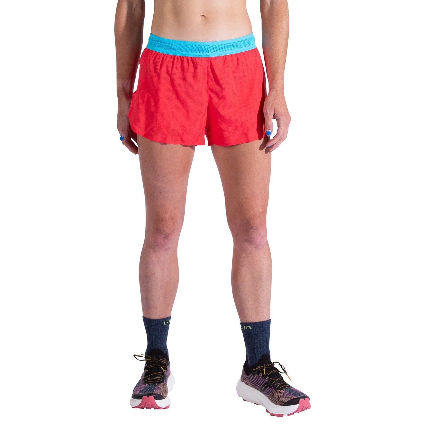 A woman models La Sportiva Pure 3 Inch Shorts in bright red with a light blue waistband, paired with dark socks and running shoes. Only her lower torso and legs are visible against a white background.