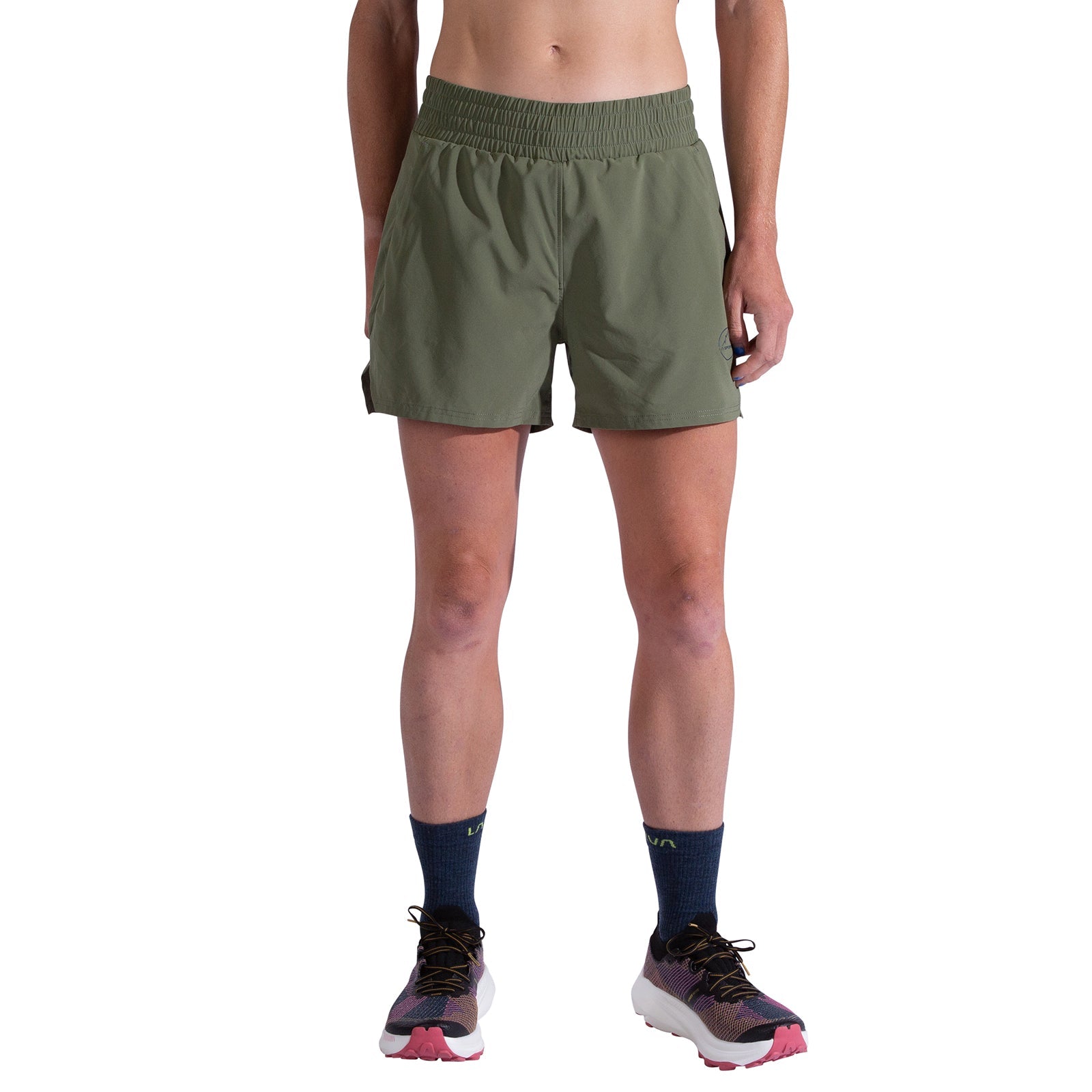 A person is shown from the waist down wearing La Sportiva Pure 4 Inch Shorts Women's in olive green, navy blue crew socks, and running shoes with pink soles, all set against a white background.