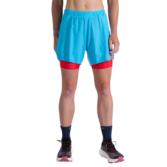 A woman stands in La Sportiva Flow 5 Inch Shorts, featuring navy socks and red compression shorts underneath. Only her lower torso and legs are shown against a white background; breathable stretch fabric ensures comfort.