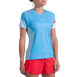 A woman stands against a white background wearing the La Sportiva Flow T-Shirt Women's in light blue with white and red accents, paired with red shorts. The sporty, short-sleeved shirt is perfect for athletes and her face is partially out of frame.