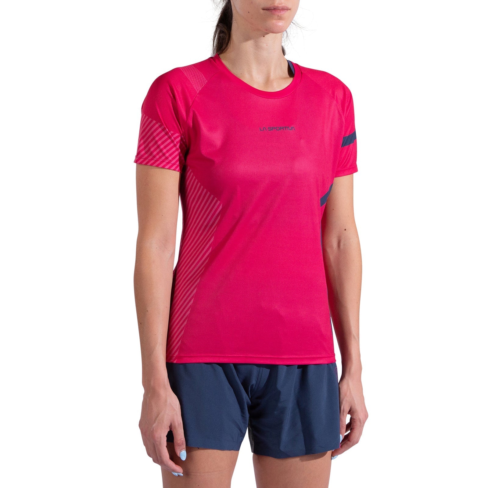 A woman wears the La Sportiva Flow T-Shirt Women's in bright pink with diagonal stripe details and navy blue shorts, standing against a plain white background.