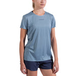 A woman wears the La Sportiva Pure T-Shirt Women's in light blue, made from recycled polyester, with navy blue shorts, standing against a plain white background. The shirt displays "La Sportiva" on the chest.