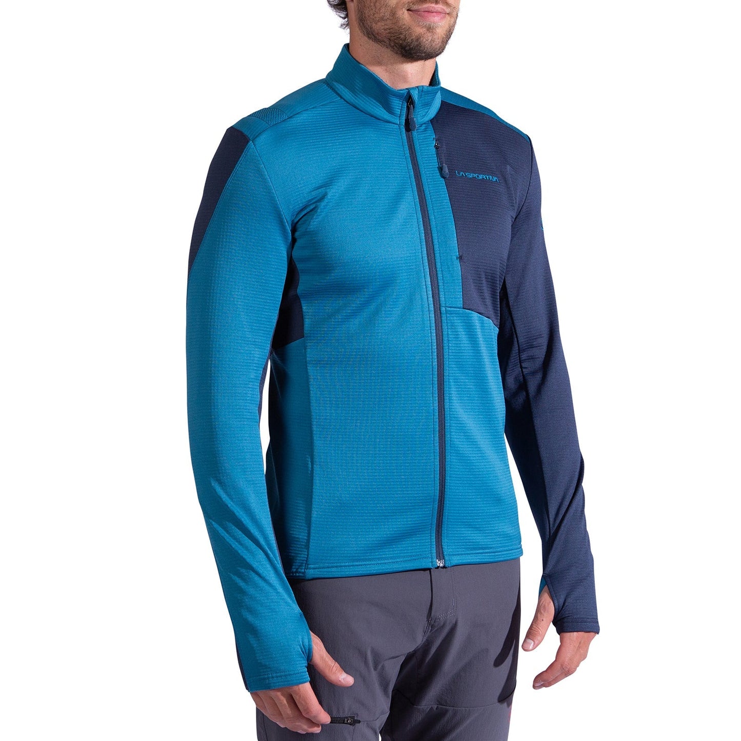 A man stands against a white background wearing the La Sportiva Chill Thermal Jacket Men's in blue/navy with long sleeves, a high collar, stretch fabric, and a chest pocket. He completes the look with gray pants.