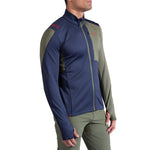 A person models the La Sportiva Chill Thermal Jacket Men's, featuring navy blue and olive green color blocks and long sleeves, paired with olive green pants, against a white background.