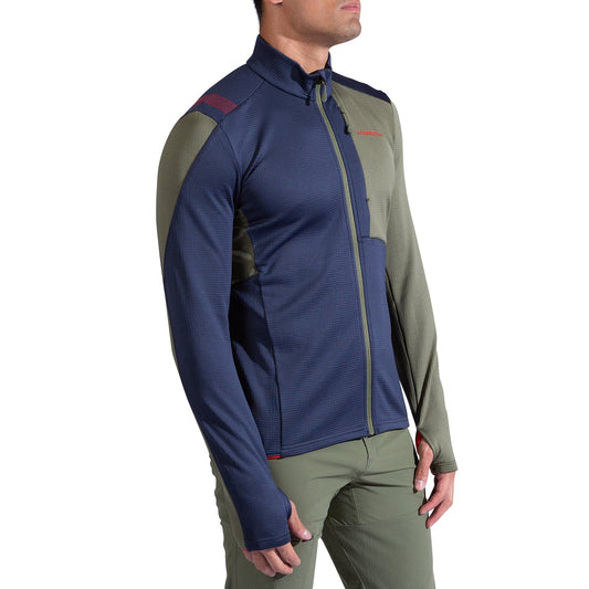 A person models the La Sportiva Chill Thermal Jacket Men's, featuring navy blue and olive green color blocks and long sleeves, paired with olive green pants, against a white background.