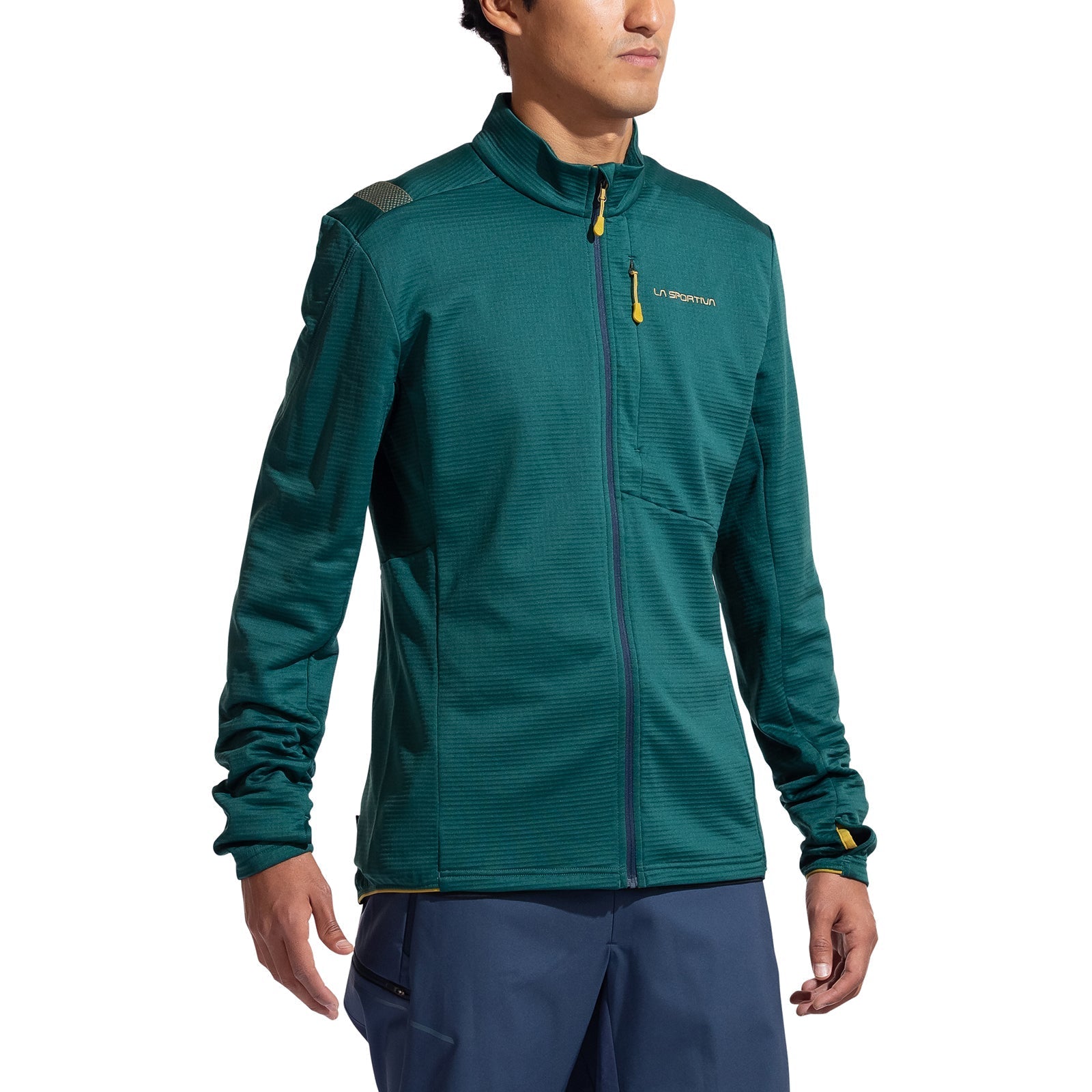 A man in a La Sportiva Chill Thermal Jacket Men's (teal, with odor control and chest pocket) and blue pants stands slightly turned on a white background.